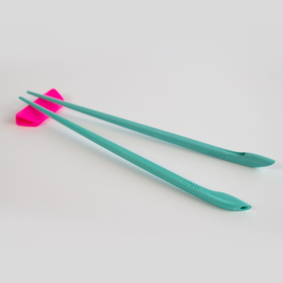 Bright teal colour chopsticks resting on a screaming pink chopstick rest. Ditokki hashi resting on hashi-oki
